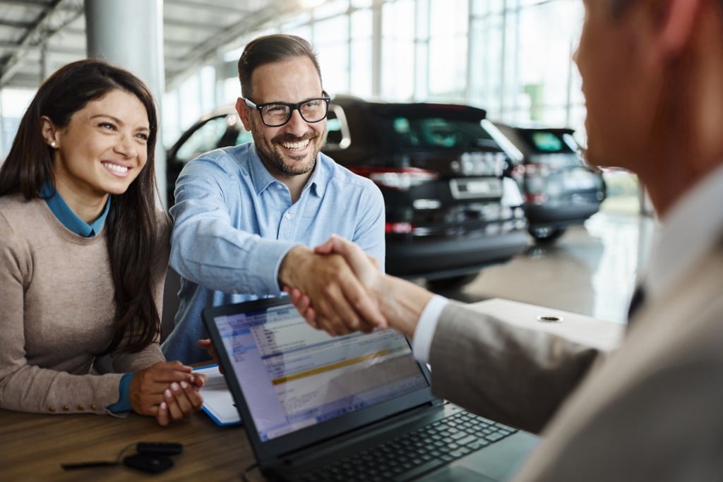 This is a photo of a car salesperson interacting with a couple.